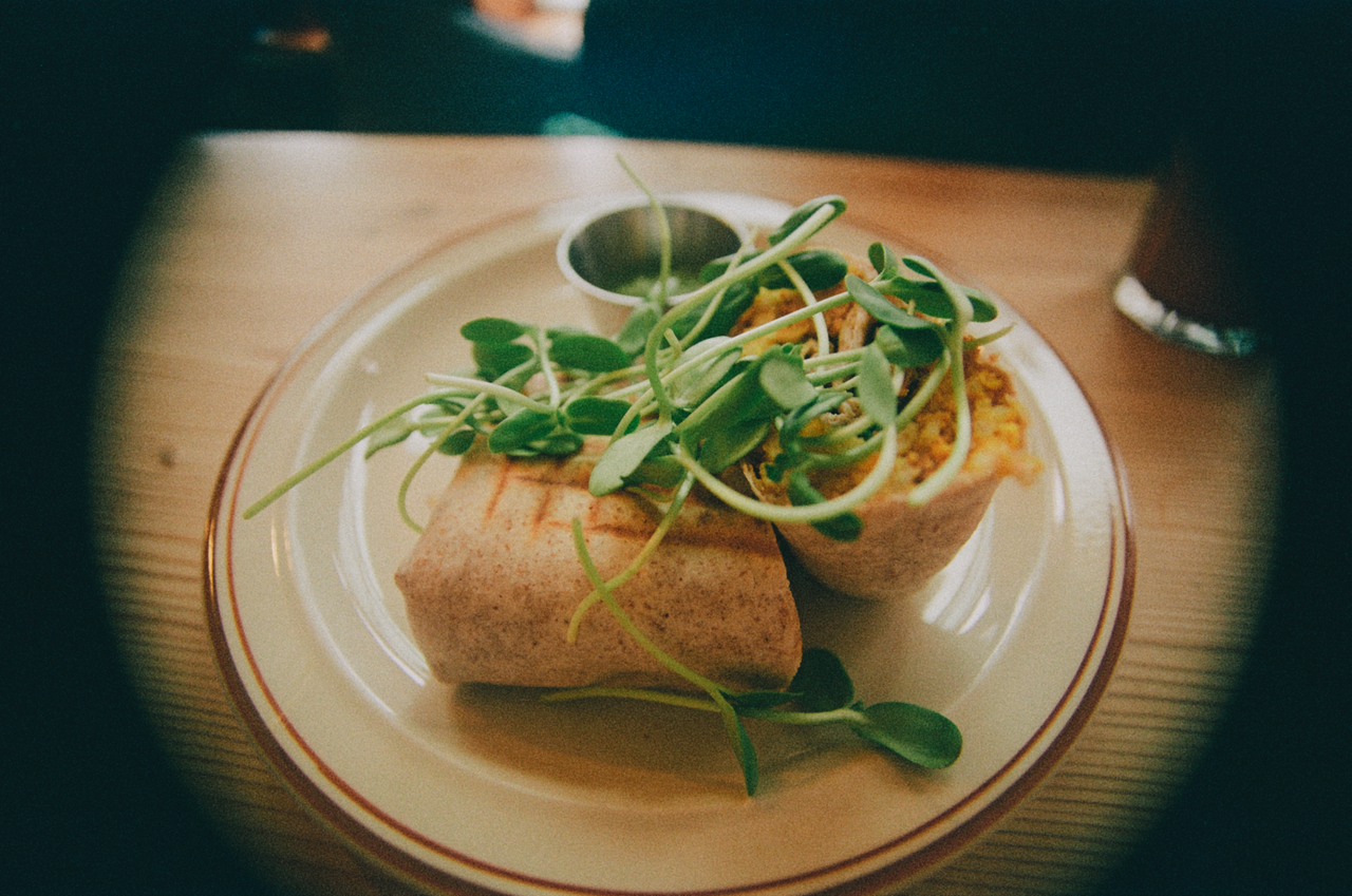 Close-up of a vegan wrap topped with fresh sprouts, shot indoors.