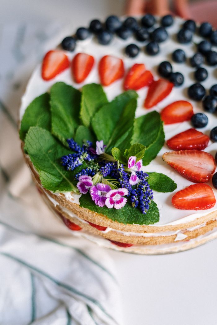 Delicious cake topped with fresh strawberries, blueberries, mint leaves, and colorful flowers.